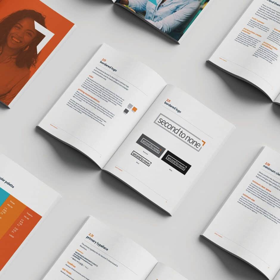 Open guidebooks with branding designs are spread on a white surface. Pages feature text, logos, and color schemes, conveying a professional tone.