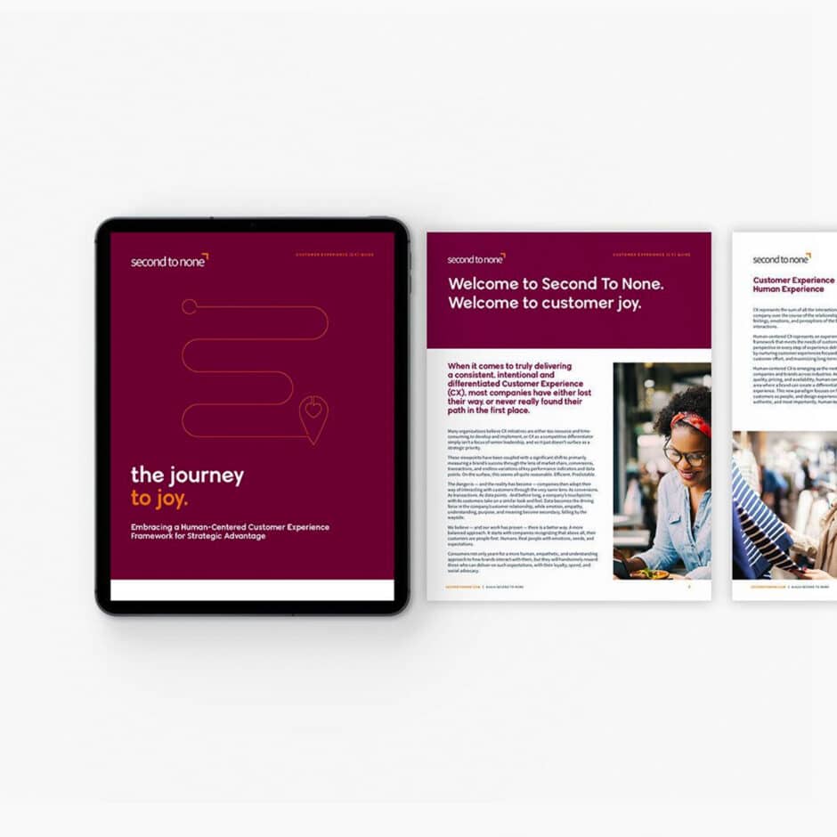 Tablet and two papers displaying "Second to None" branding with maroon and white theme. Includes text: "The journey to joy" and a smiling person image.
