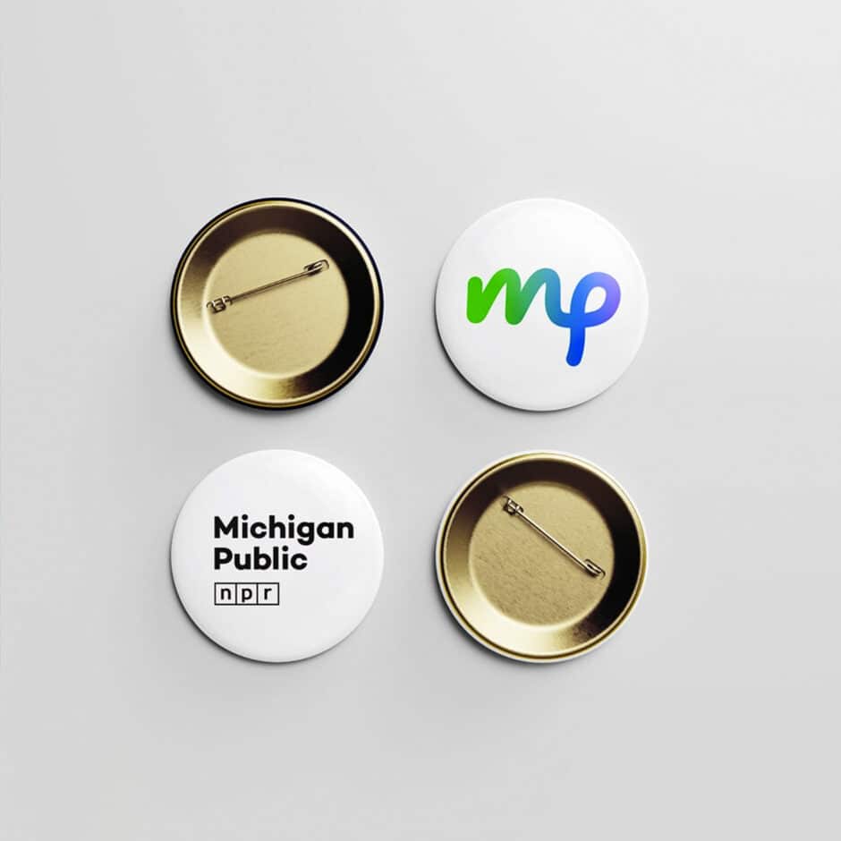 Four round buttons on a white background. Two face up showing designs: "mp" in green and blue, and "Michigan Public" with "npr" logo. Two face down, showing their gold pin backs.