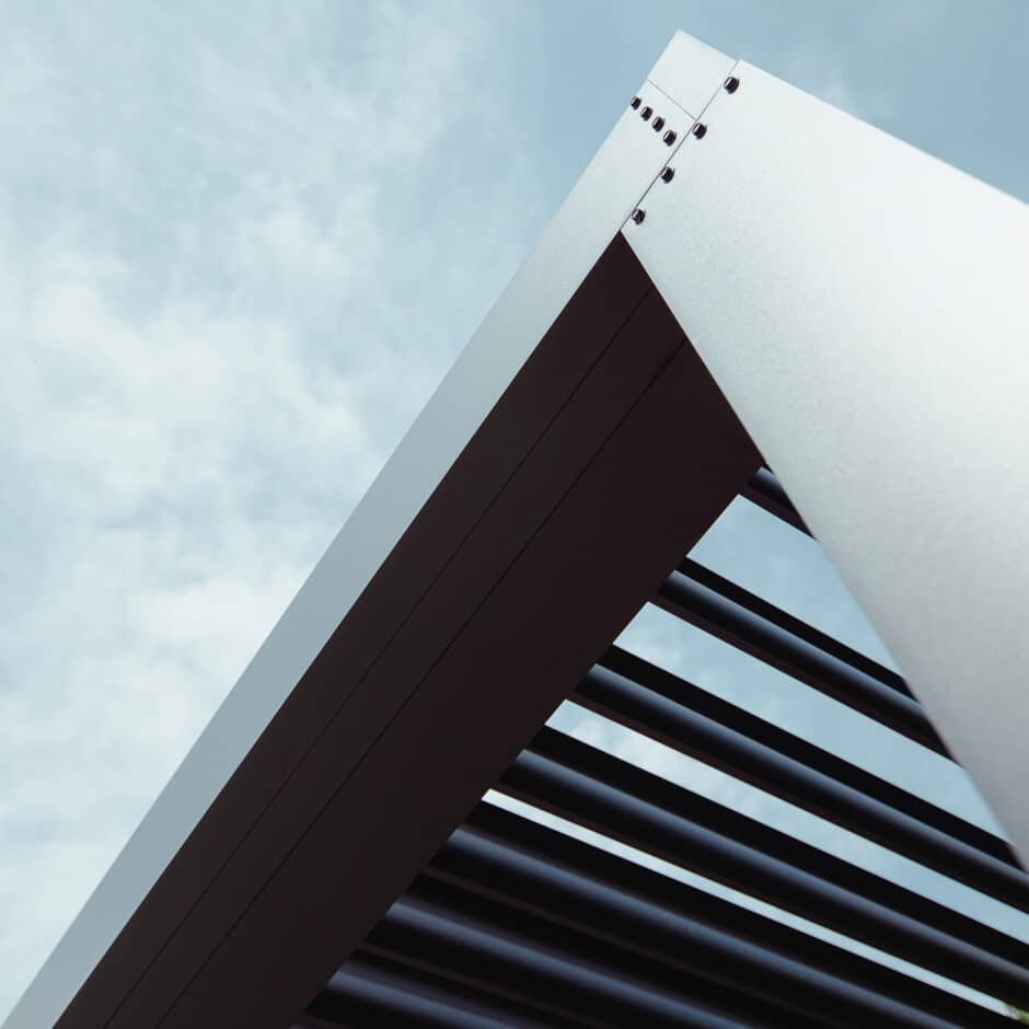 Close-up of a modern architectural structure with sleek metal beams forming a geometric pattern against a cloudy sky, conveying a sense of minimalism and sophistication.