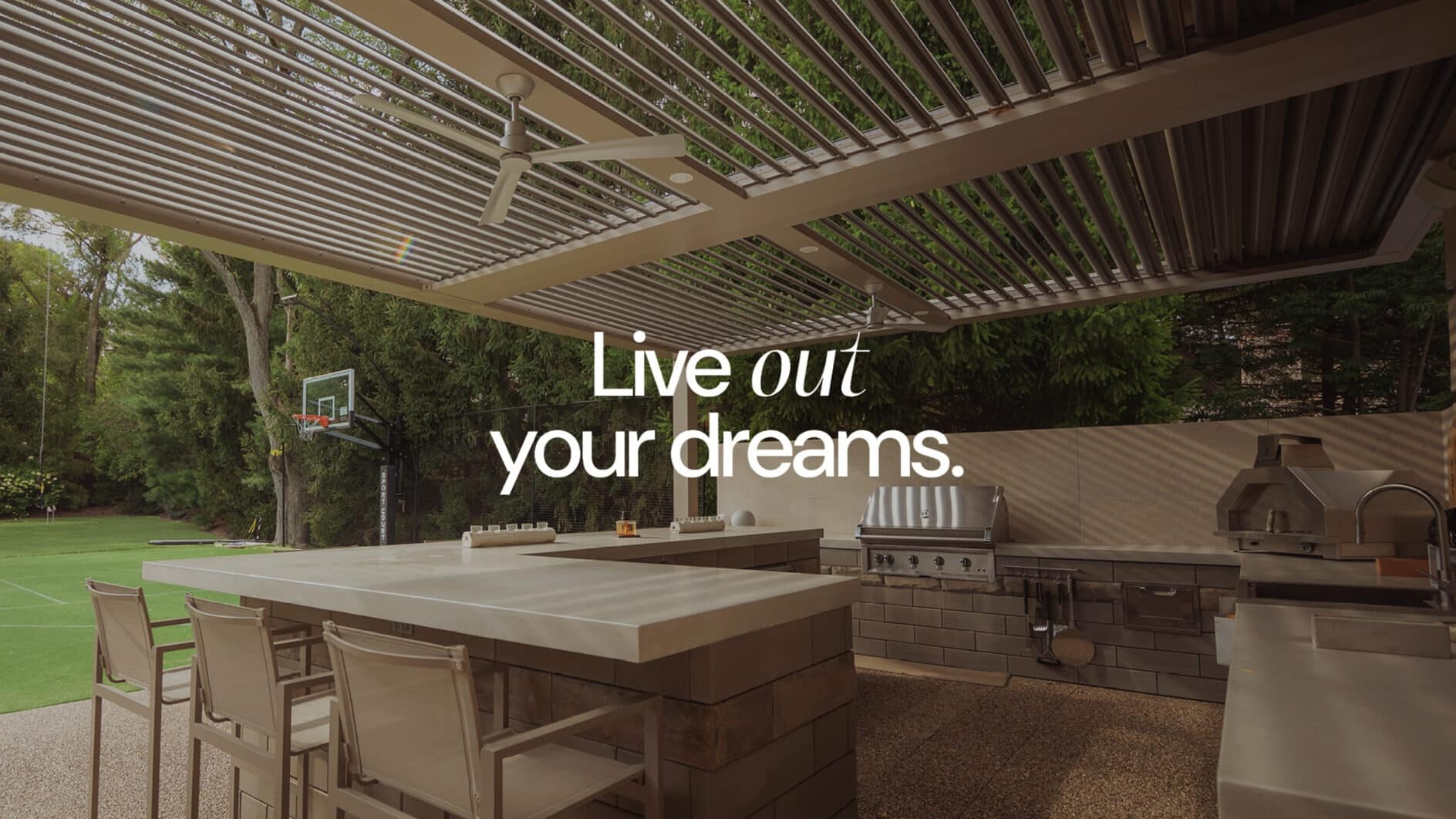 Outdoor kitchen with modern appliances under a pergola, near a tennis court, surrounded by trees. Text overlays read "Live out your dreams." Luxurious and inviting atmosphere.