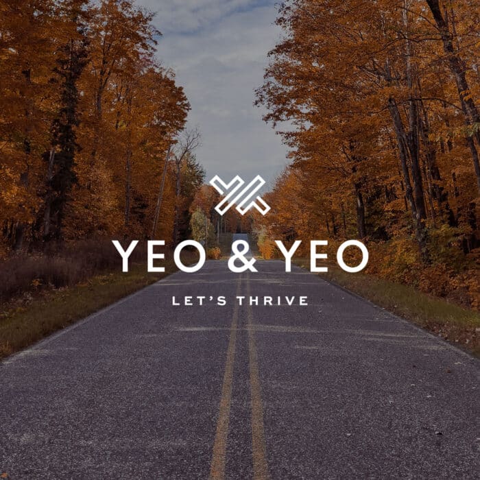 Road flanked by vibrant autumn trees leads into the distance. Text overlay reads "Yeo & Yeo" with slogan "Let's Thrive," conveying growth and optimism.